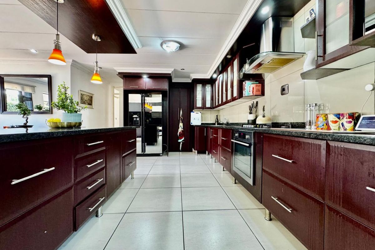 Modern kitchen featuring dark wood cabinetry, granite countertops, built-in oven, stainless steel extractor fan, and tiled flooring with a central island.