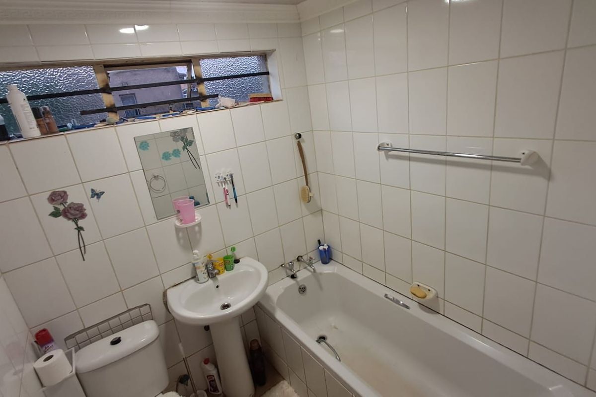 A dated bathroom featuring a pedestal basin, bathtub with shower mixer, and tiled walls, requiring some maintenance and cosmetic updates.