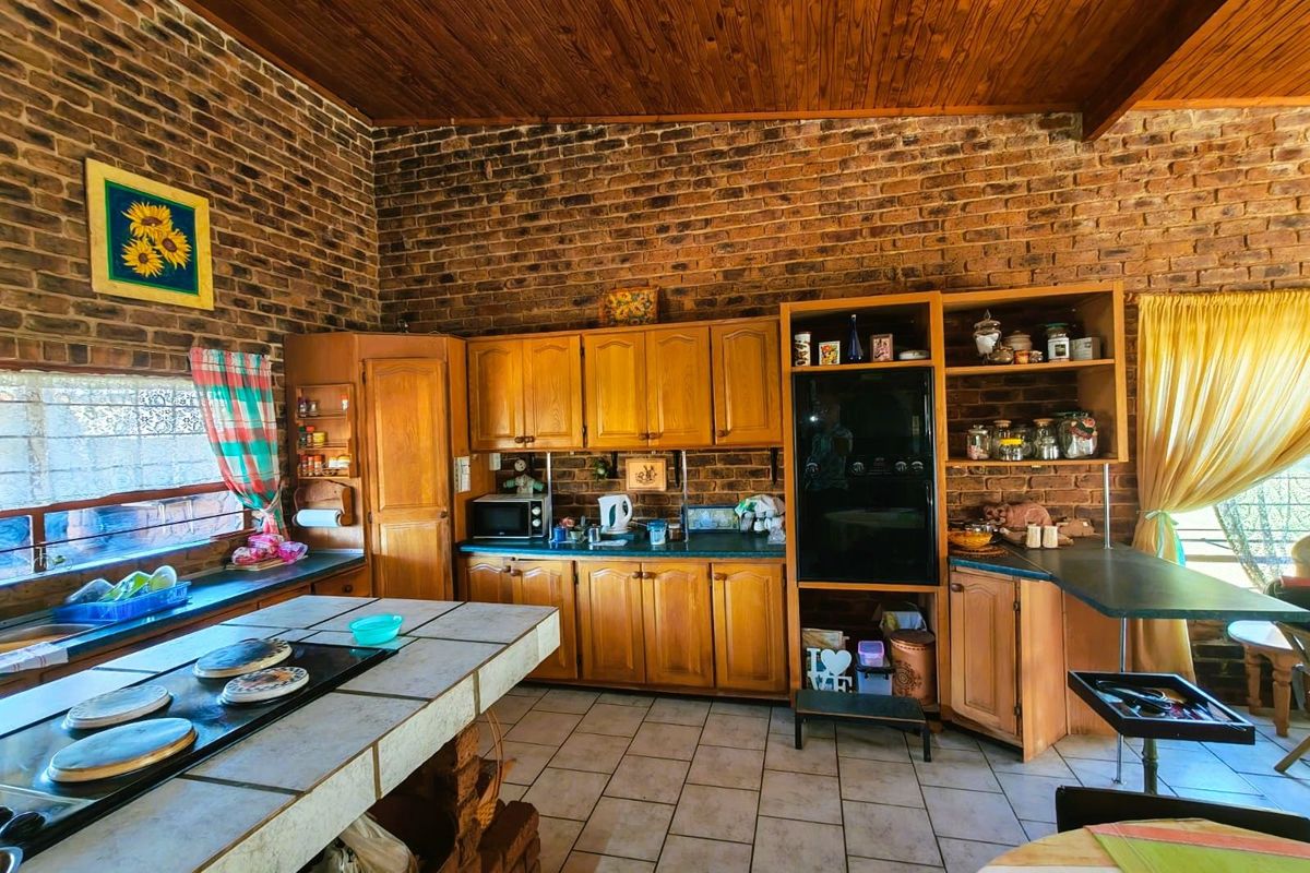 A rustic kitchen featuring exposed brick walls, timber ceiling, tiled island countertop, and traditional wooden cabinetry with integrated oven and hob.