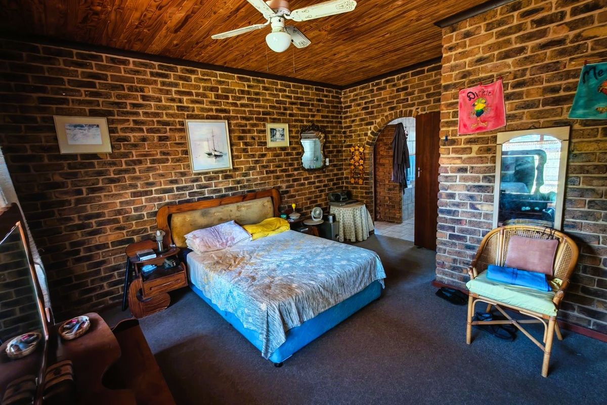 A bedroom featuring exposed face-brick walls, a timber-clad ceiling with a central fan, and an arched doorway leading to an adjoining space.