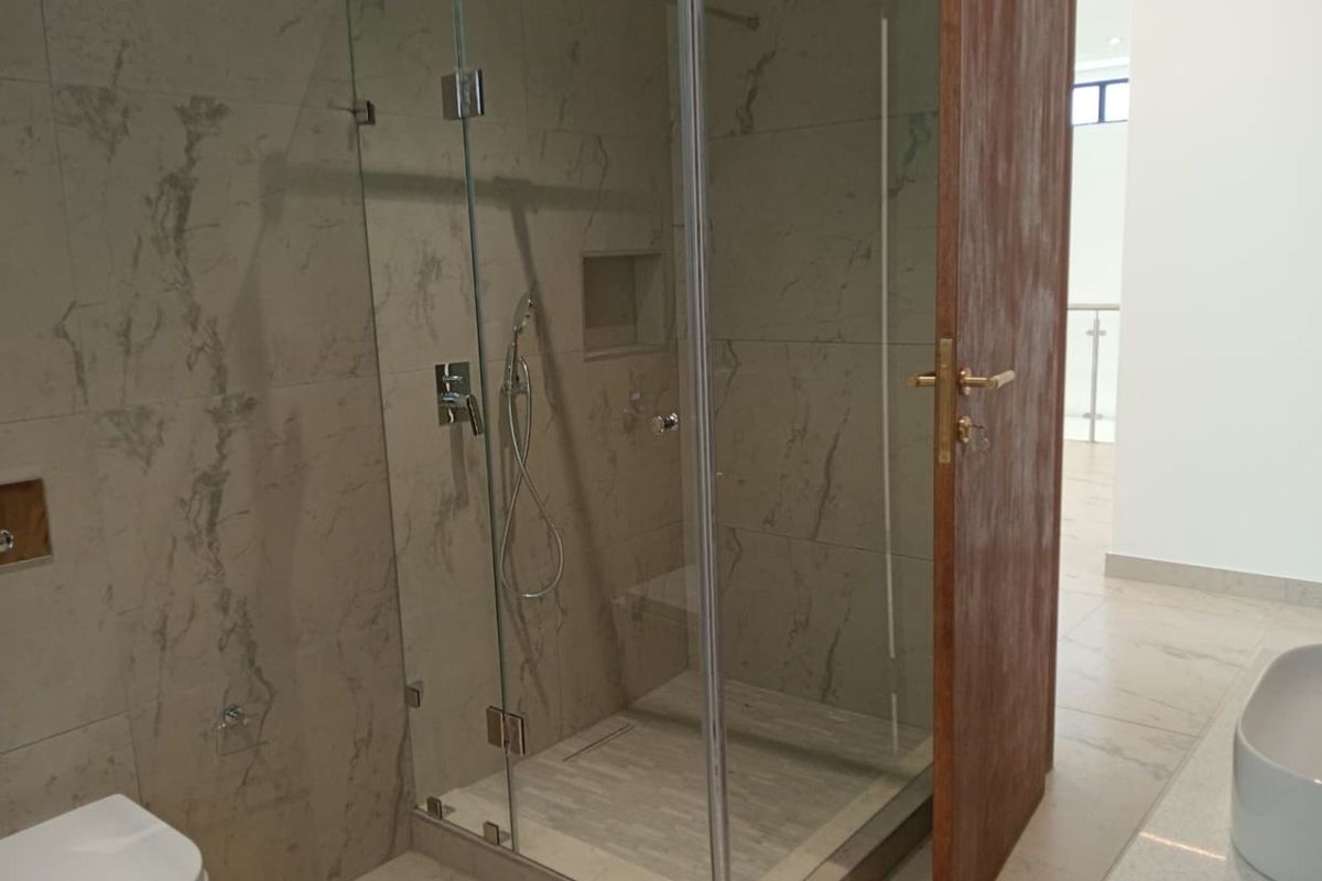 Modern bathroom featuring a frameless glass walk-in shower with marble-look wall tiles, a built-in shower niche, and high-quality chrome fixtures.