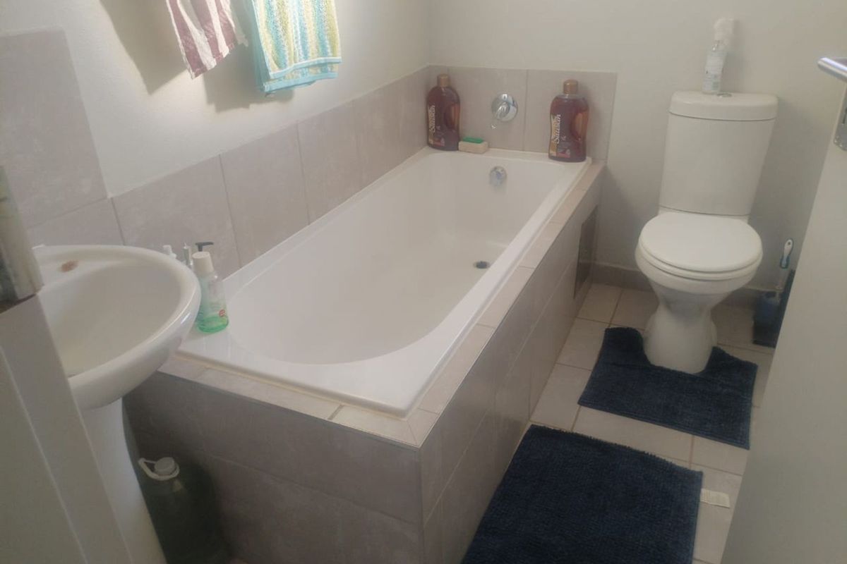 A functional bathroom featuring a built-in bathtub with tiled surround, a pedestal basin, and a standard toilet.