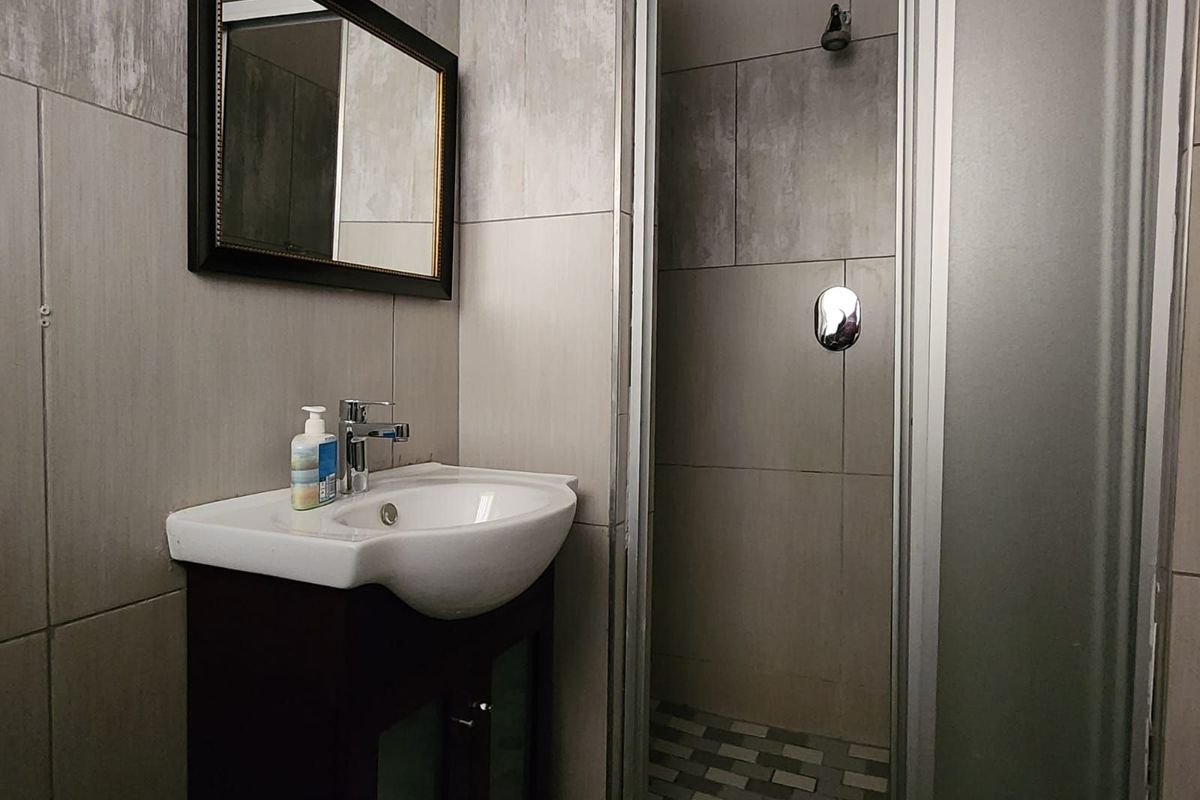A functional bathroom featuring a vanity basin with a wall-mounted mirror and a separate shower enclosure with tiled walls and flooring.