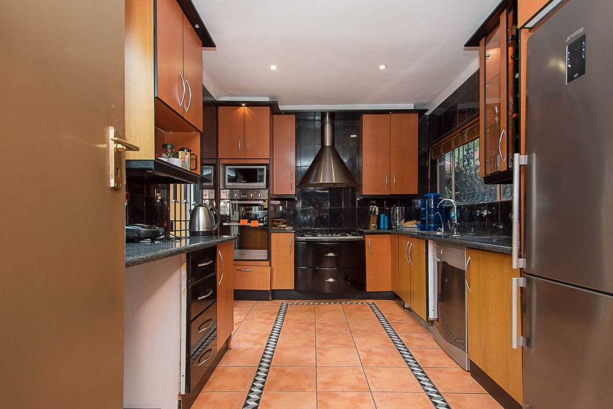 A functional kitchen featuring wood-toned cabinetry, dark granite countertops, a stainless steel extractor fan, and integrated oven with a tiled floor.
