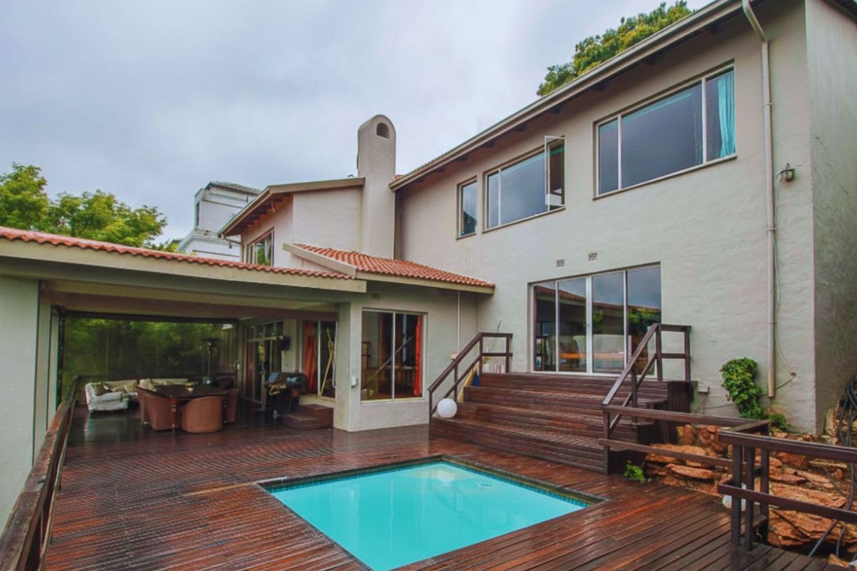 Rear view of the property featuring a swimming pool, expansive timber decking, covered patio area, and multi-level access stairs.