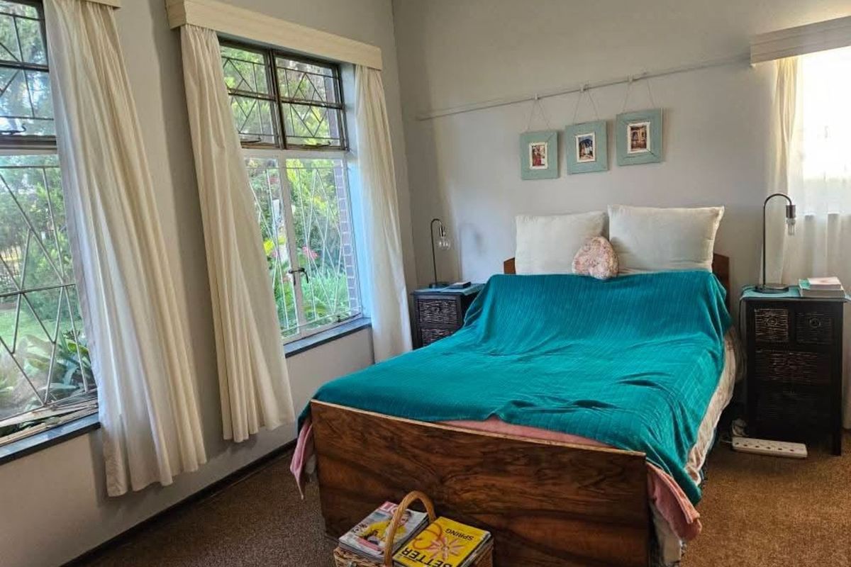 A cozy bedroom featuring leaded glass windows, neutral wall finishes, and carpeted flooring, providing a comfortable and well-lit living space.