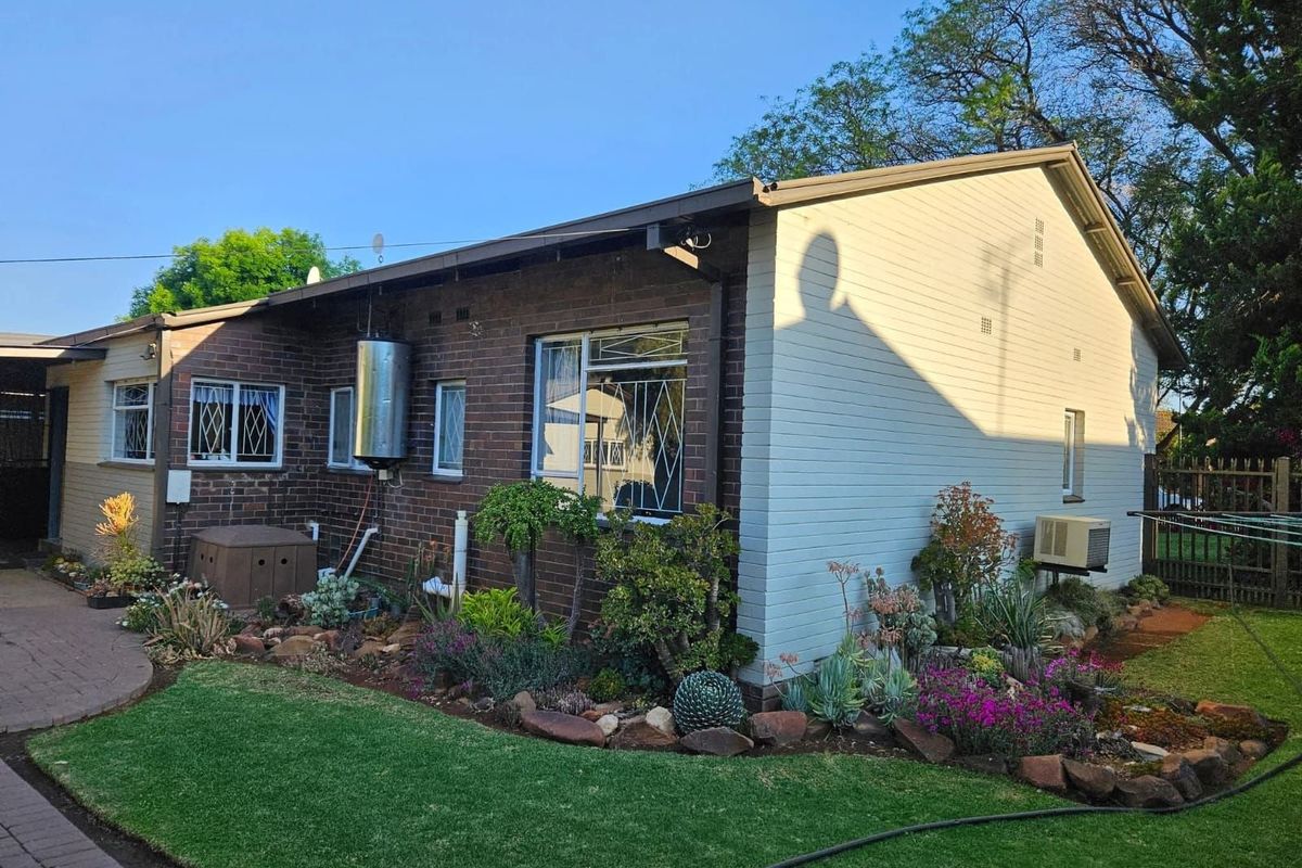 Rear exterior view of the house featuring brick and siding facade, landscaped garden beds, and an external geyser unit.