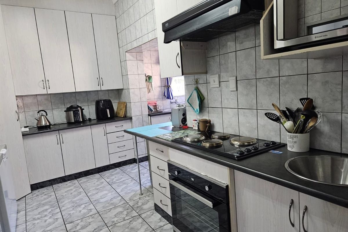 Functional kitchen featuring built-in cabinetry, integrated oven, hob, extractor fan, and tiled surfaces with a connected scullery area.