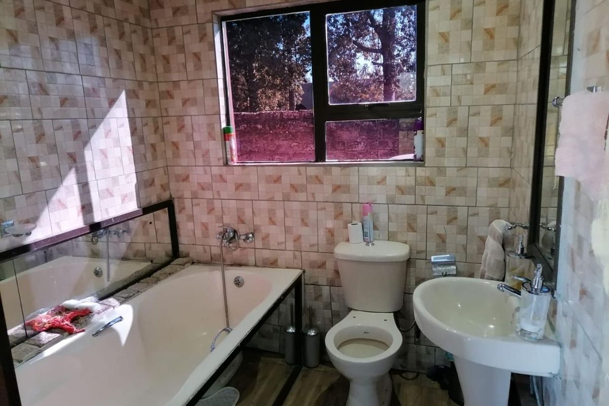 A functional bathroom featuring a built-in bathtub, pedestal basin, and toilet, finished with patterned wall tiles and a window for natural light.