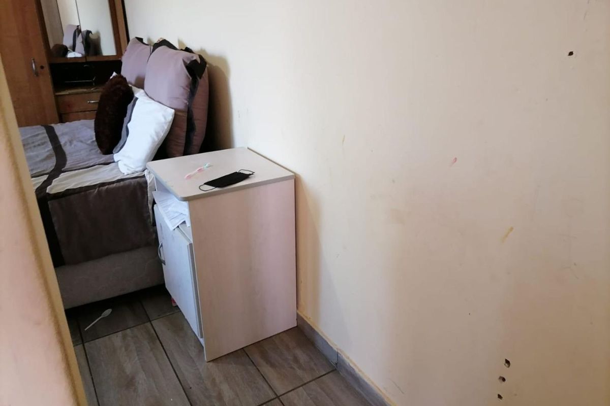 A bedroom featuring tiled flooring and plain wall finishes, showing signs of wear and surface damage requiring maintenance.