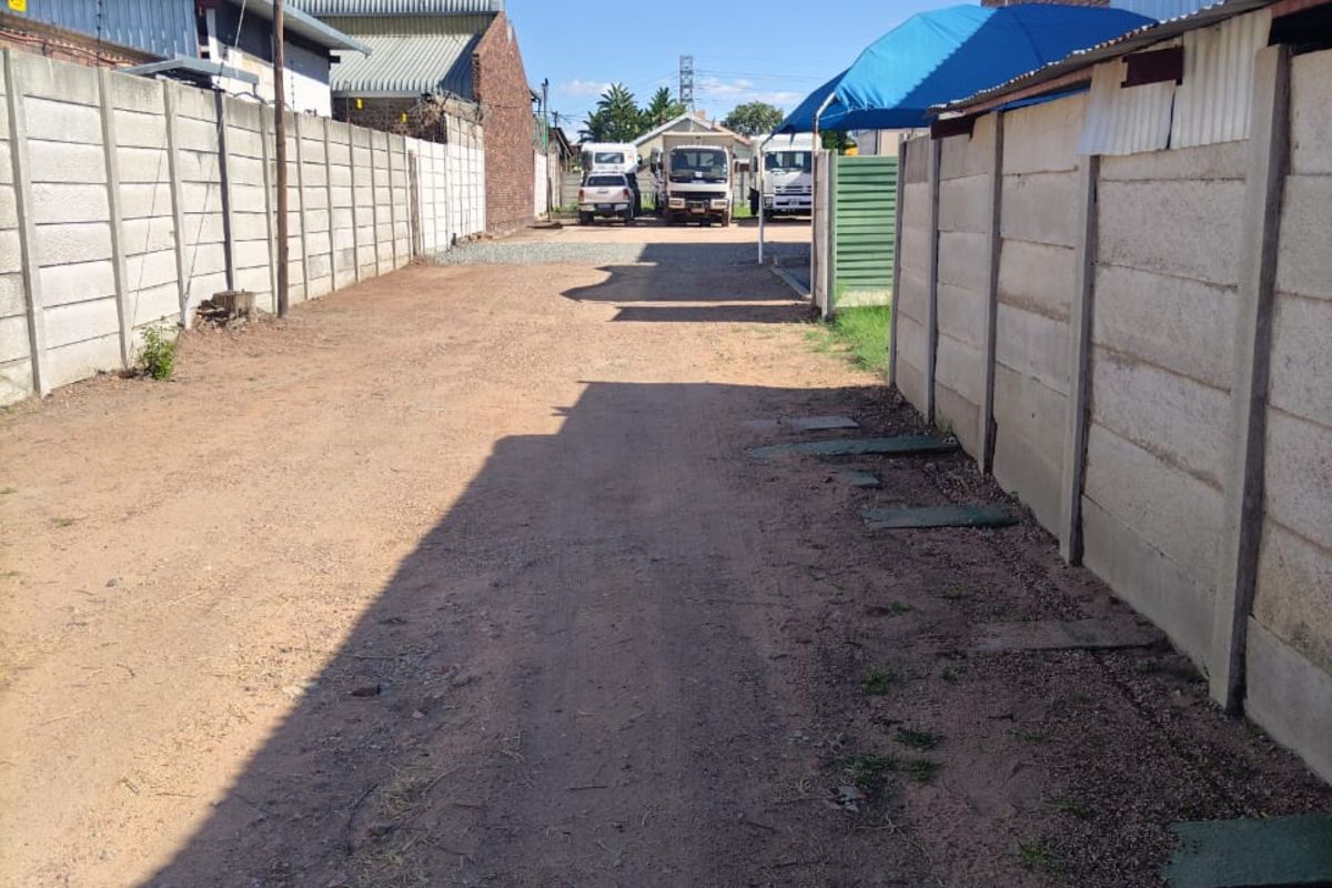 Commercial property access driveway featuring precast concrete boundary walls and an unpaved gravel surface leading to the rear yard area.