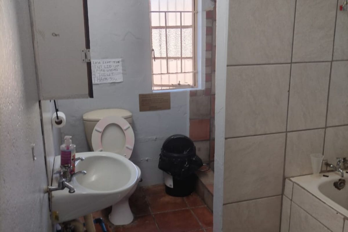 A functional bathroom featuring a bathtub, toilet, and wall-mounted basin with tiled flooring and a privacy partition wall.