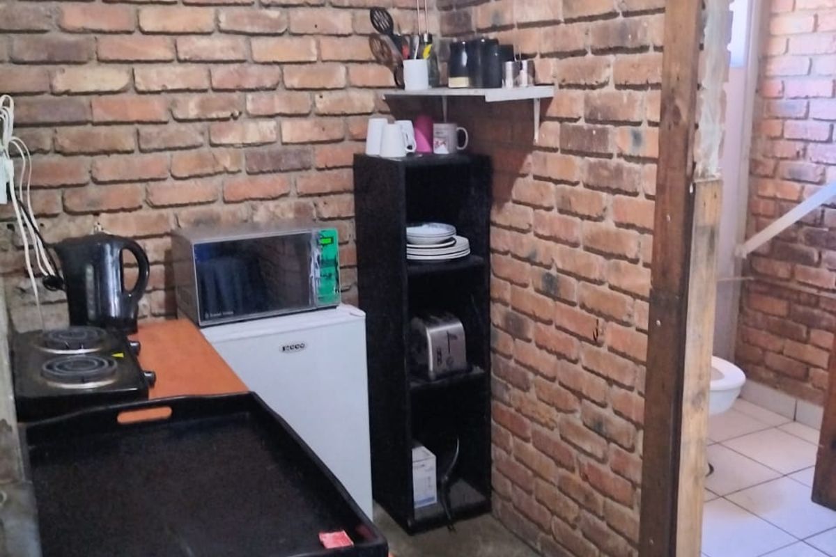 A basic kitchenette area featuring exposed brick walls and concrete flooring, with an adjacent bathroom visible through an unfinished doorway.