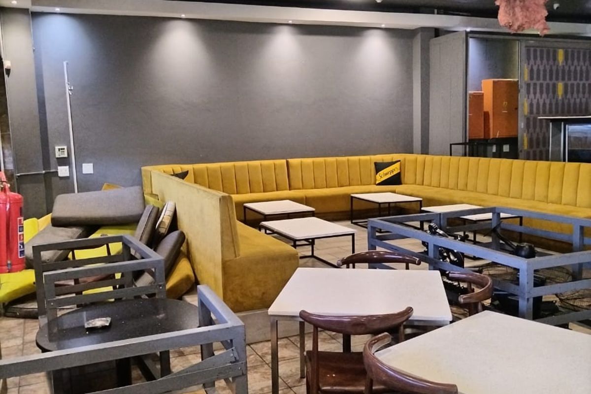Commercial lounge area featuring built-in yellow banquette seating, recessed ceiling lighting, and tiled flooring, currently showing signs of wear and ceiling damage.