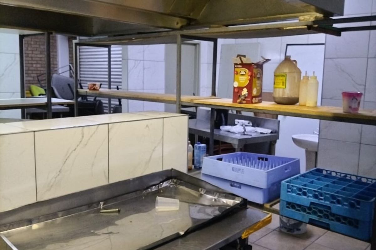 Commercial kitchen area featuring stainless steel prep surfaces, a large overhead extractor hood, and tiled flooring.