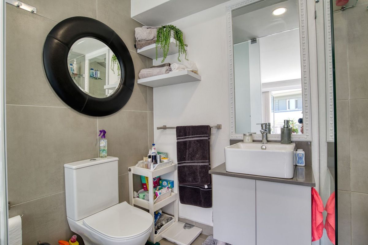 A modern bathroom featuring a vessel sink vanity, wall-mounted mirror, toilet, and neutral large-format wall tiling.
