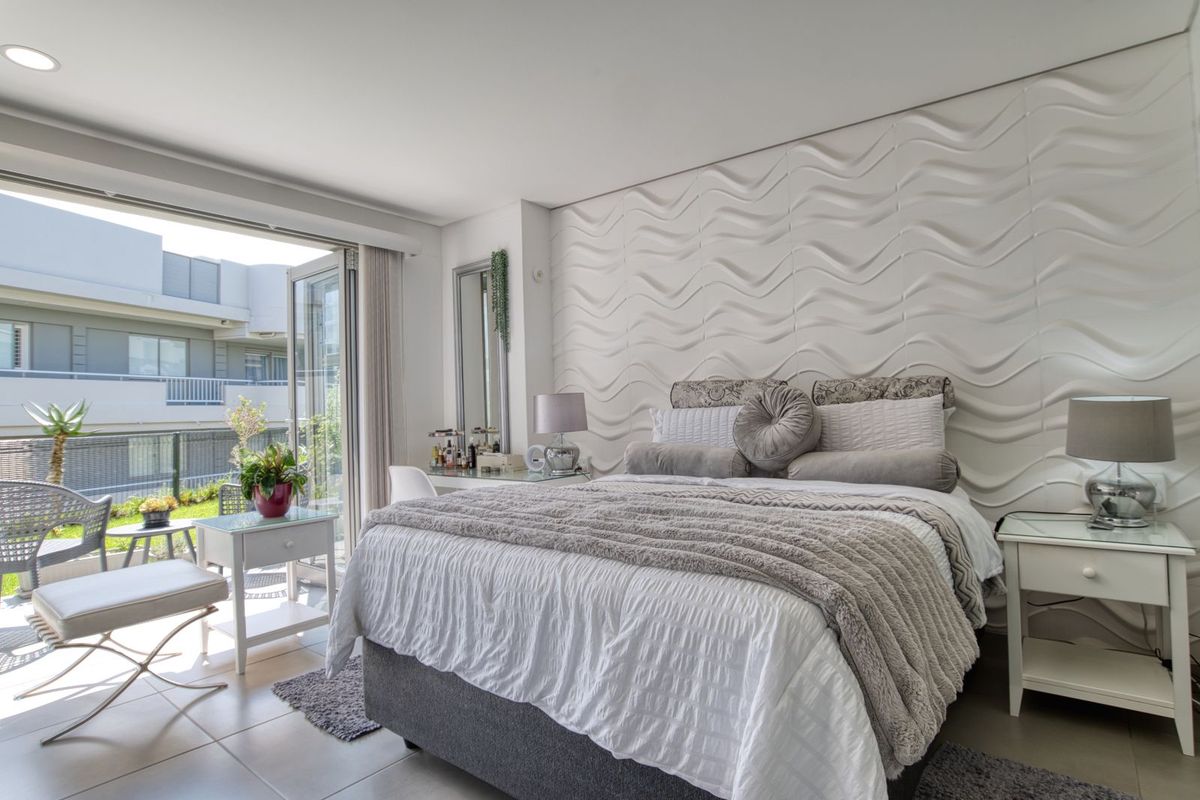 Modern bedroom featuring a textured feature wall, tiled flooring, and large sliding glass doors opening onto a private balcony.