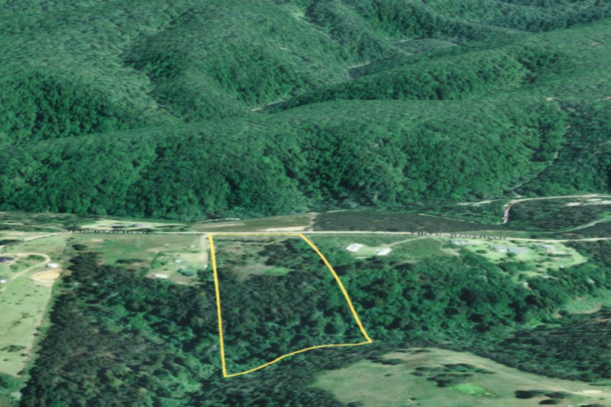An aerial view of a vacant residential land parcel, highlighting the property boundaries against a backdrop of rolling hills and natural landscape.