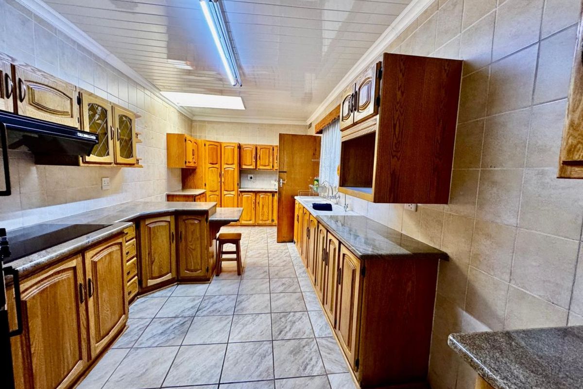 A spacious kitchen featuring extensive wooden cabinetry, tiled flooring, and wall tiling, offering a functional layout with ample storage and counter space.