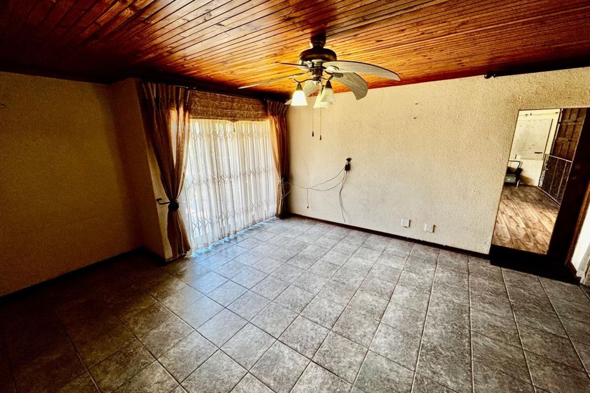 A living room featuring tiled flooring, a timber-clad ceiling with a central fan, and sliding glass doors with security gates.
