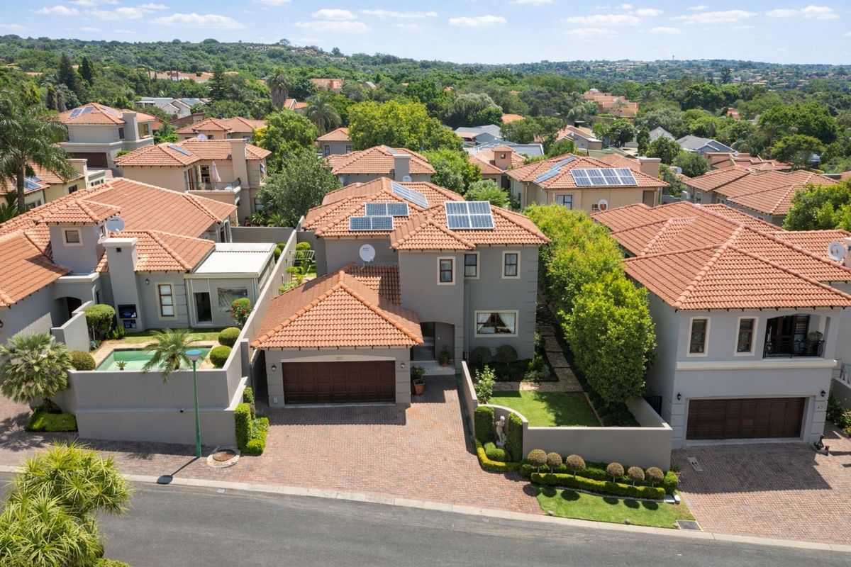 Aerial view of a residential property featuring a tiled roof, solar panels, a paved driveway, a garage, and a private swimming pool.