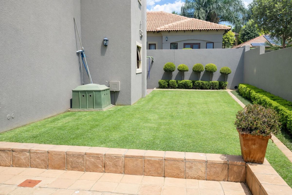 A well-maintained rear garden featuring a manicured lawn, perimeter boundary walls, and a paved patio area.