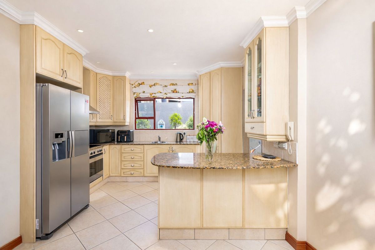 A functional kitchen featuring light wood cabinetry, granite countertops, a breakfast bar, and tiled flooring with integrated oven and extractor fan.