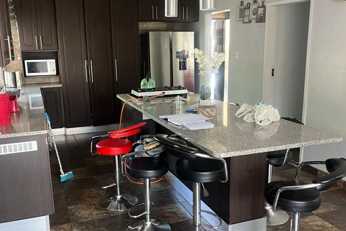 Spacious kitchen featuring dark wood cabinetry, granite countertops, a central breakfast island with pendant lighting, and tiled flooring throughout.