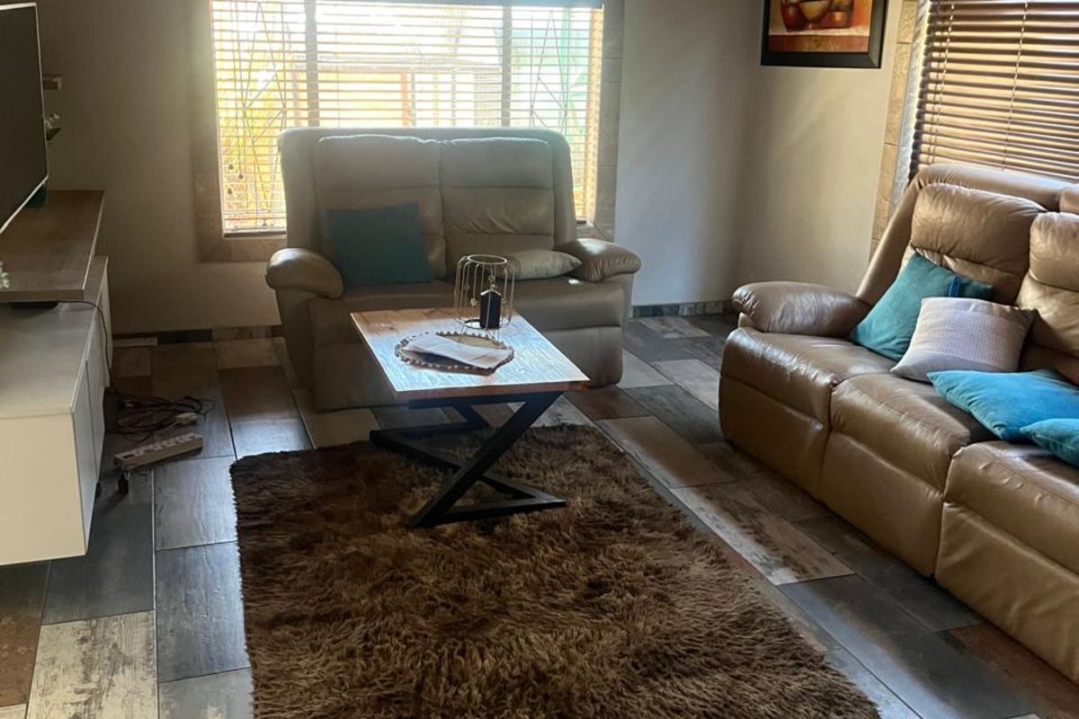 A cozy living room featuring rustic wood-paneled ceilings, multi-toned wood-look floor tiles, and large windows with fitted blinds.
