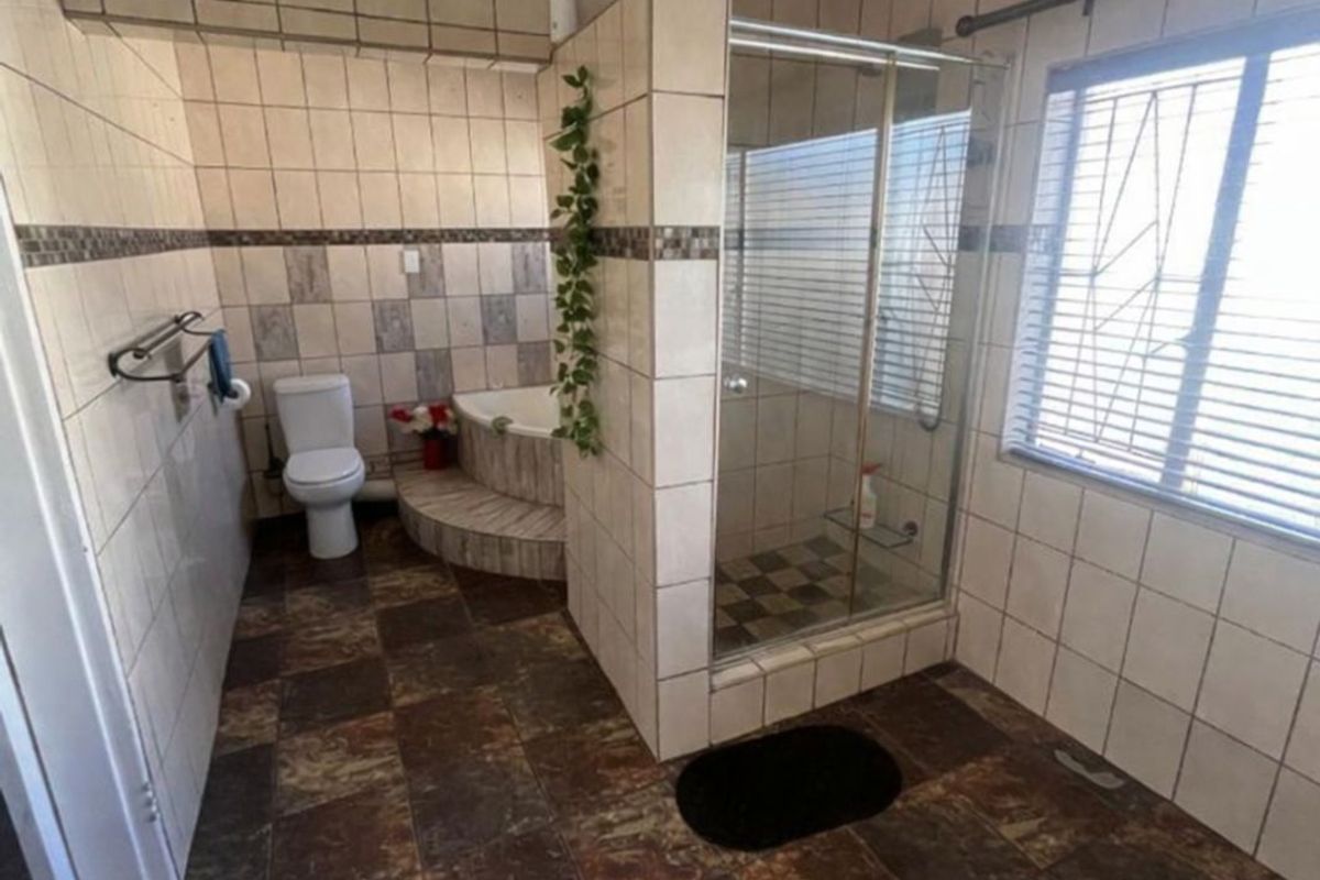 A bathroom featuring a glass-enclosed shower, a corner bathtub, and a toilet, finished with dark slate-style floor tiles and neutral wall tiling.