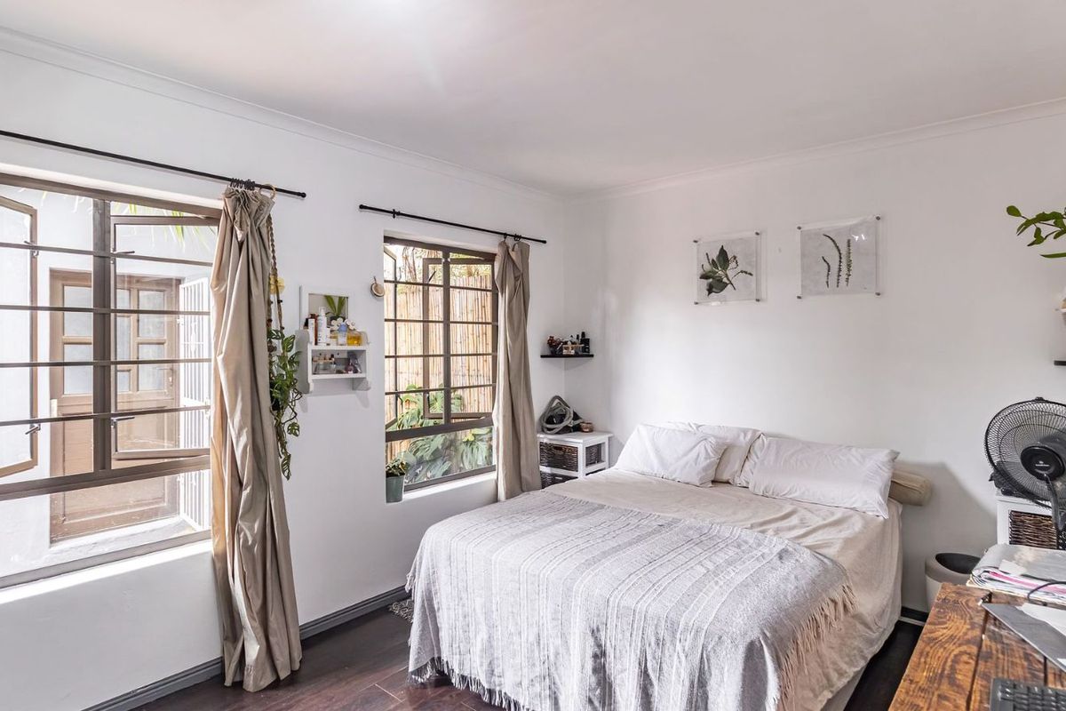 A bright bedroom featuring dark wood-look flooring, large windows with security bars, and neutral wall finishes.