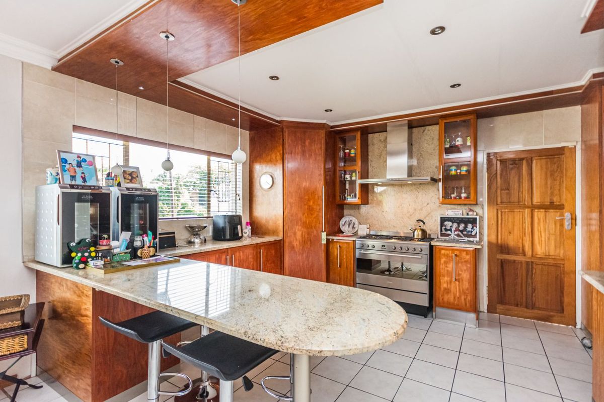 A spacious kitchen featuring granite countertops, a breakfast bar, wooden cabinetry, and a stainless steel gas stove with an extractor fan.