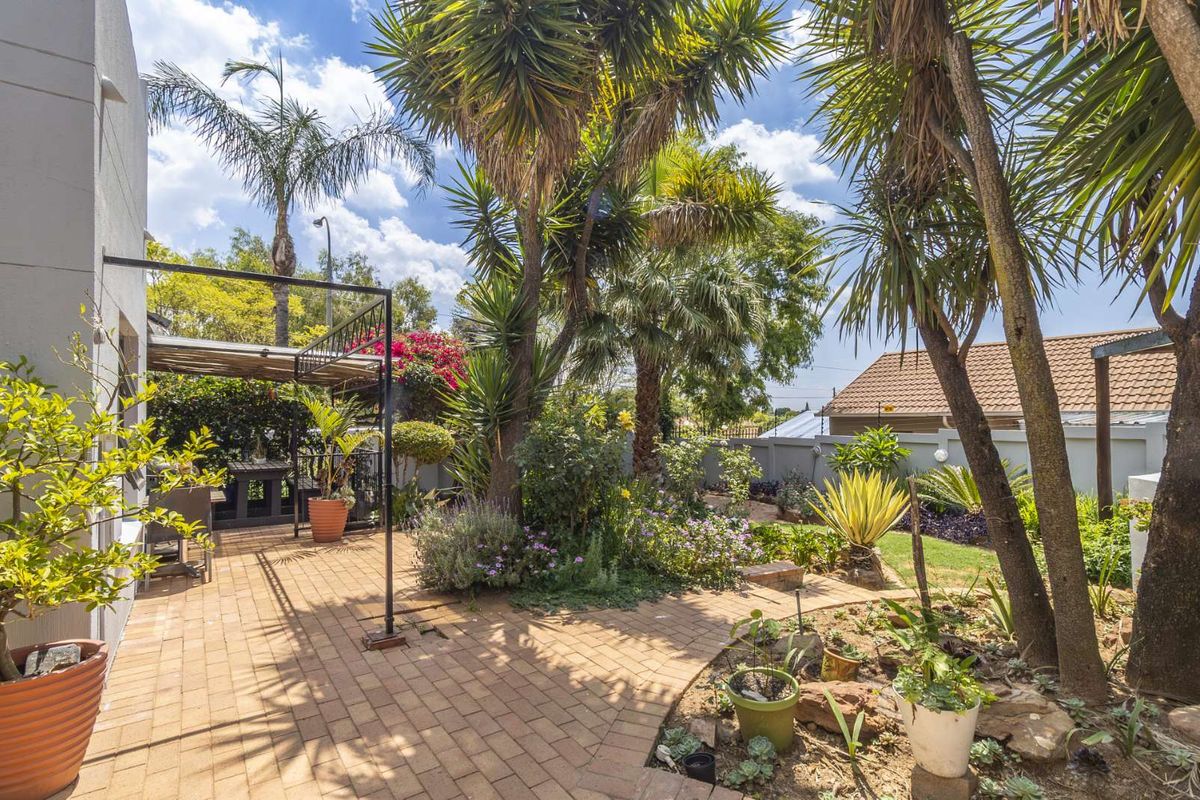 A well-maintained rear garden featuring a paved patio area, established trees, and landscaped garden beds.