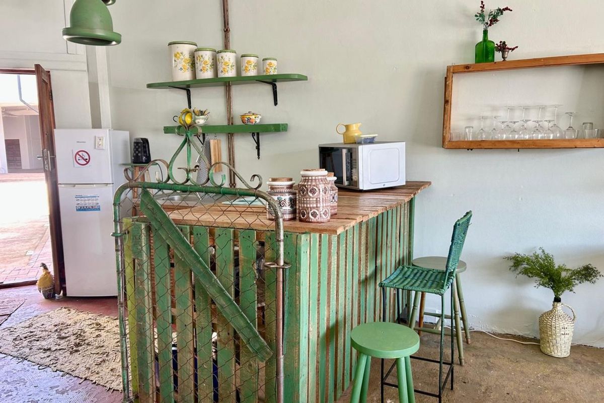 A rustic kitchen area featuring a custom-built timber counter, open shelving, and a concrete floor, offering a unique, informal prep and dining space.