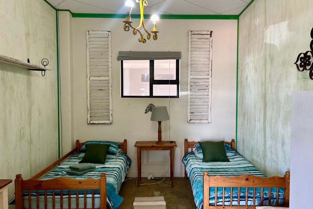 A bedroom featuring twin beds, a central window with decorative shutters, and a vintage-style chandelier.