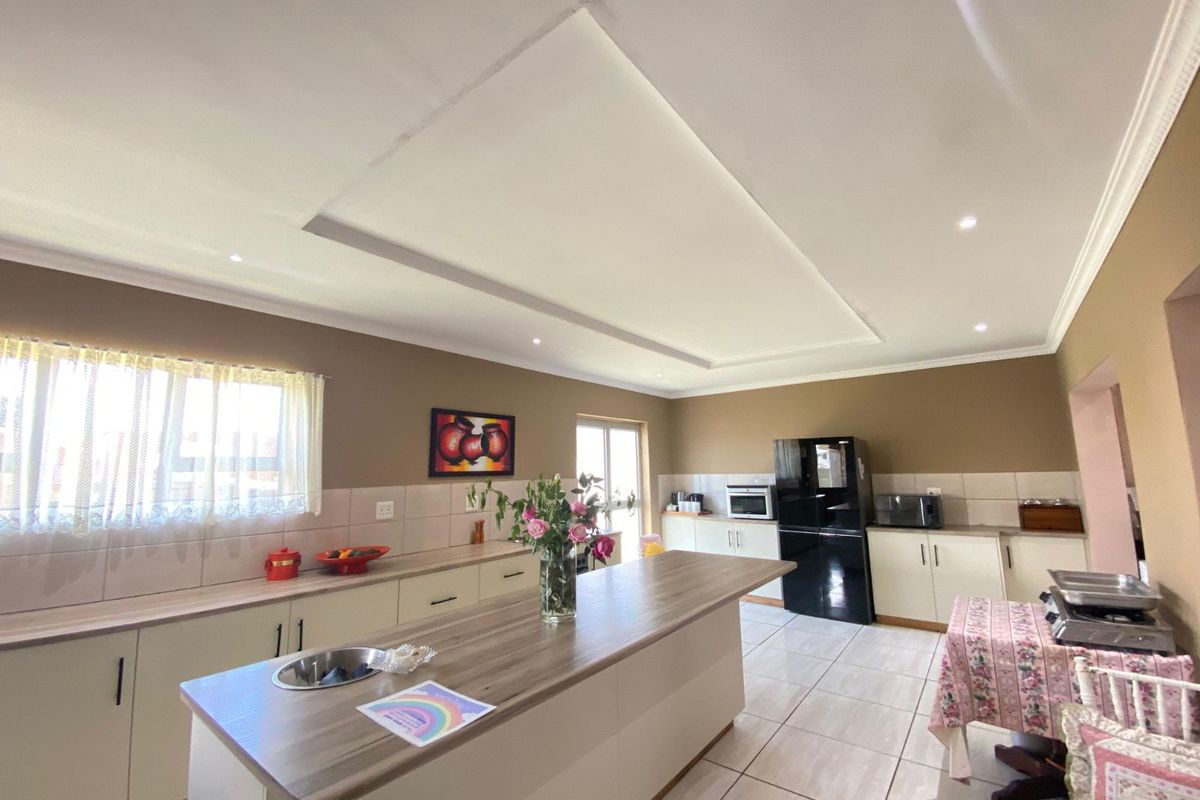 Spacious kitchen featuring a central island with a prep sink, ample cabinetry, tiled flooring, and a recessed ceiling design with integrated lighting.