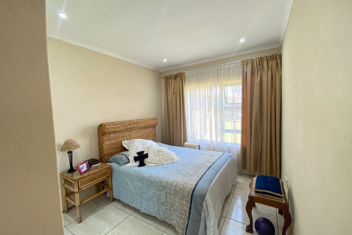 A well-lit bedroom featuring neutral tiled flooring, recessed ceiling lighting, and large windows with floor-to-ceiling curtains.
