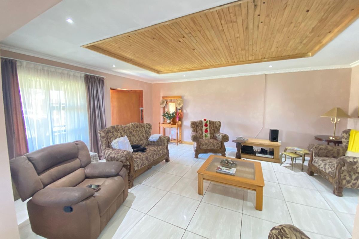 A spacious living room featuring light-colored floor tiles and a distinctive wooden panelled ceiling with recessed lighting.