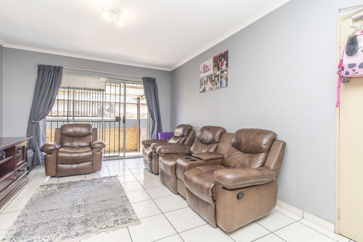 A bright living room featuring tiled flooring and a sliding glass door providing access to an outdoor patio area.