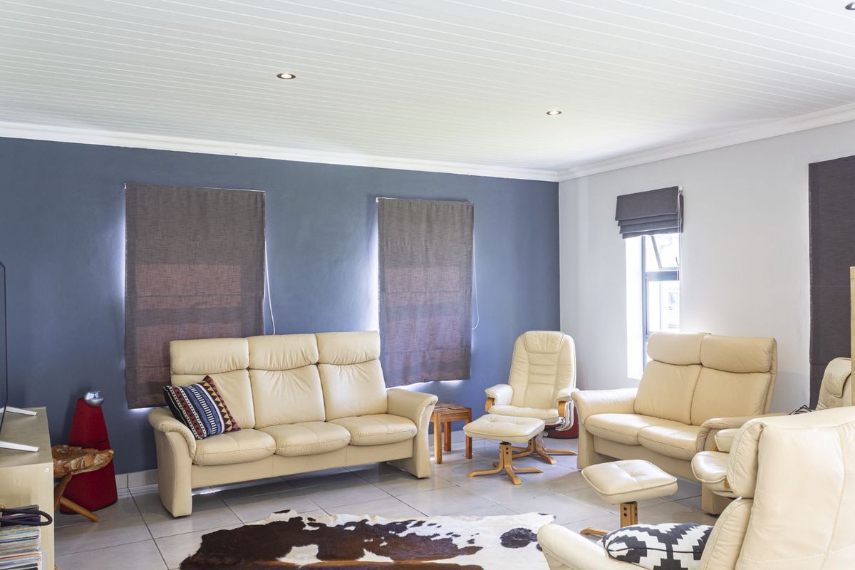 A bright and spacious living room featuring tiled flooring, recessed ceiling lighting, and a contrasting feature wall.