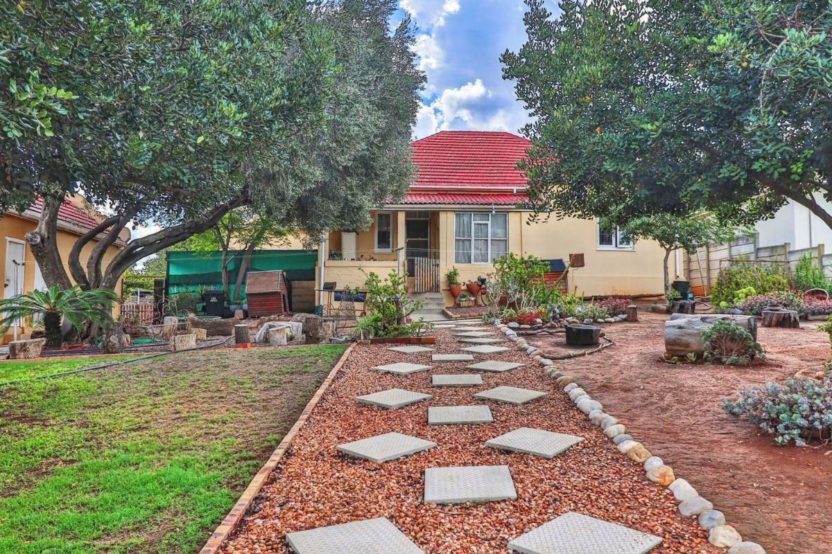 A rear view of the house featuring a garden path with stone pavers, established trees, and a red tiled roof.