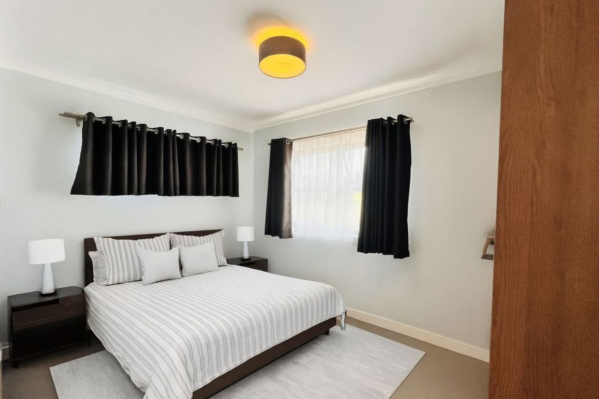 A well-maintained bedroom featuring neutral wall tones, carpeted flooring, and a central ceiling light fixture.