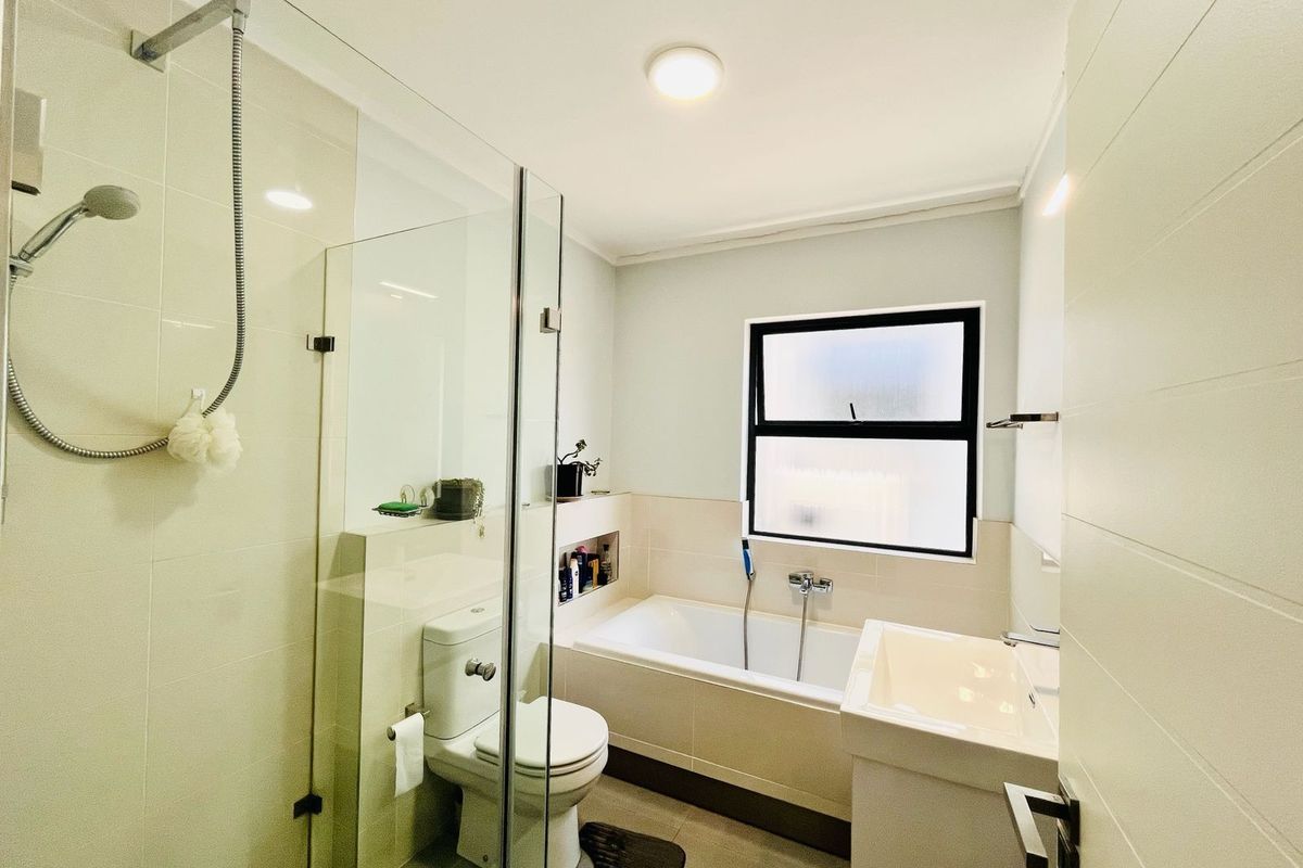 Modern bathroom featuring a glass-enclosed shower, a built-in bathtub, a pedestal sink, and a frosted window for privacy.
