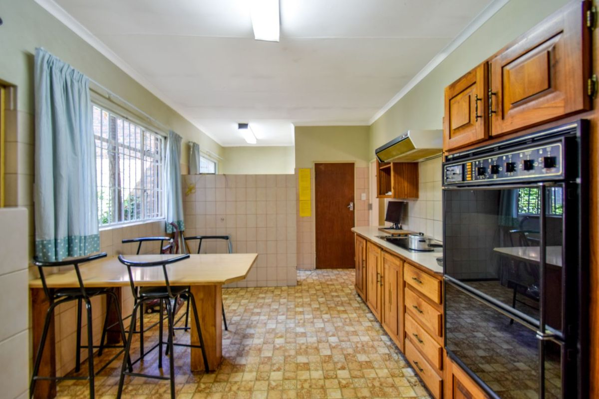 A dated kitchen featuring wooden cabinetry, a built-in double oven, extractor fan, and tiled flooring with an integrated breakfast bar area.