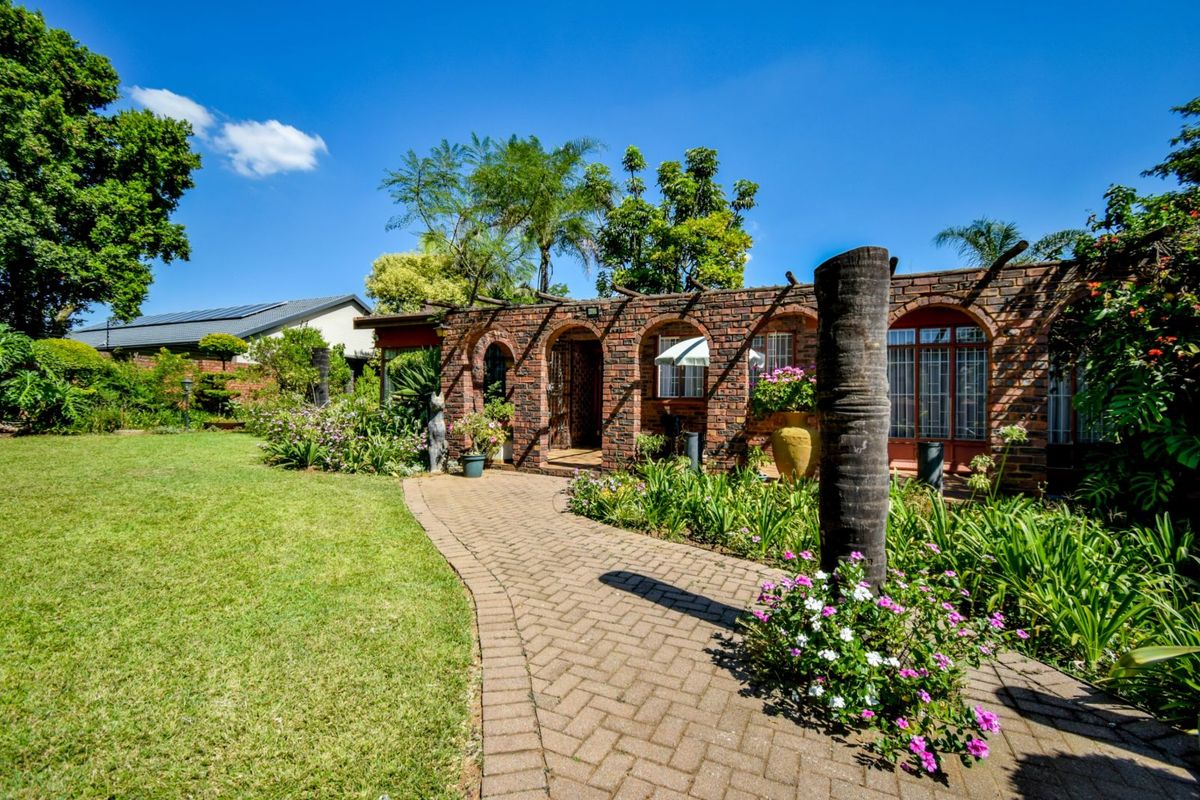 A charming rear garden featuring a brick-paved pathway leading to a rustic brick facade with arched entryways and a timber pergola structure.