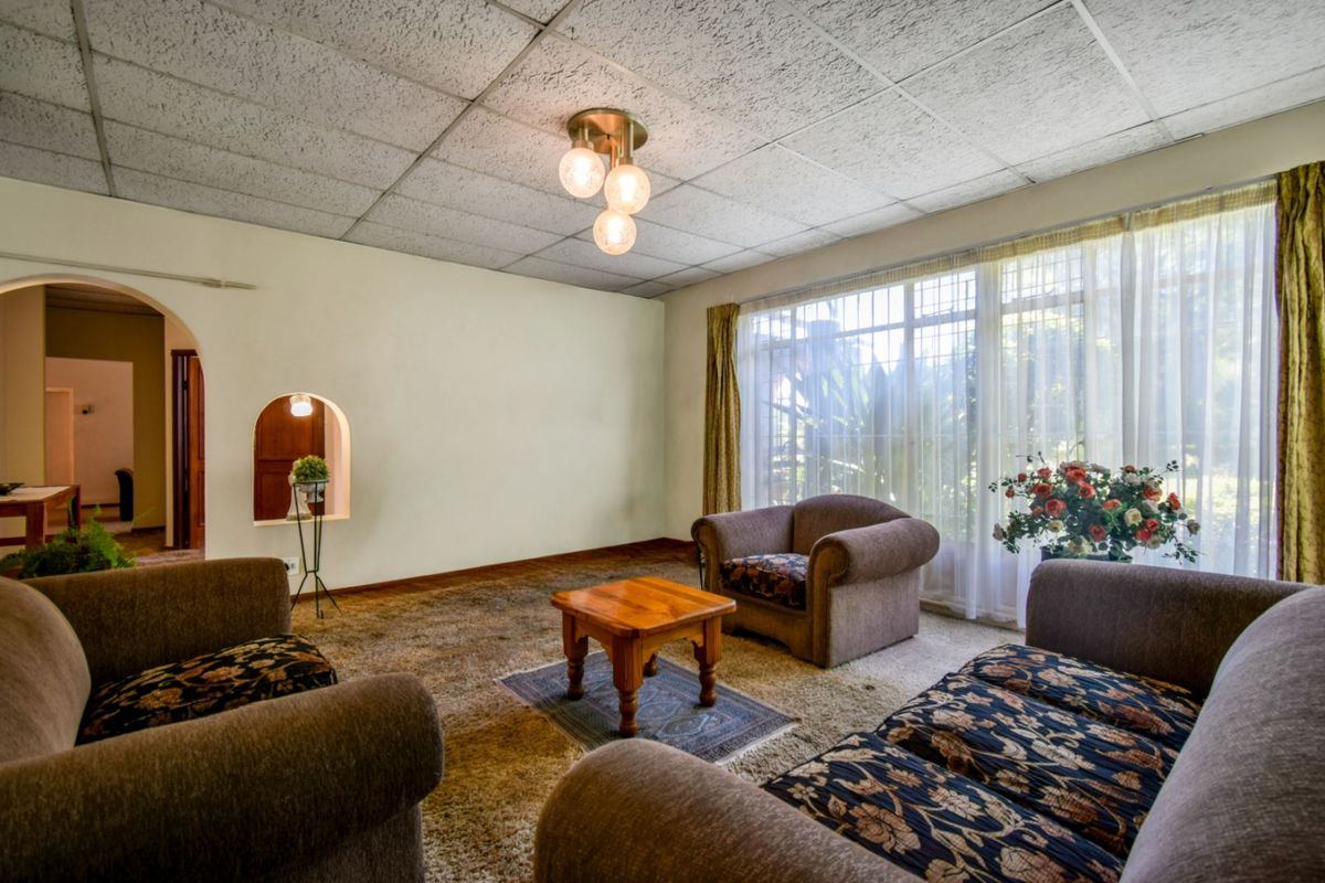 A spacious living room featuring large windows, a distinctive arched wall niche, and a drop-tile ceiling, offering a classic layout with potential for modernization.