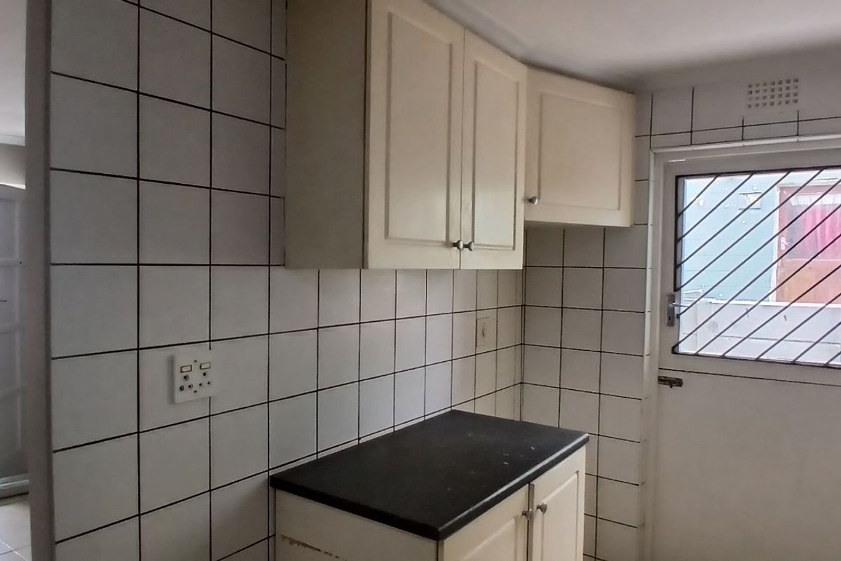 A functional kitchen area featuring tiled walls, built-in cabinetry with dark countertops, and a security gate on the exterior door.