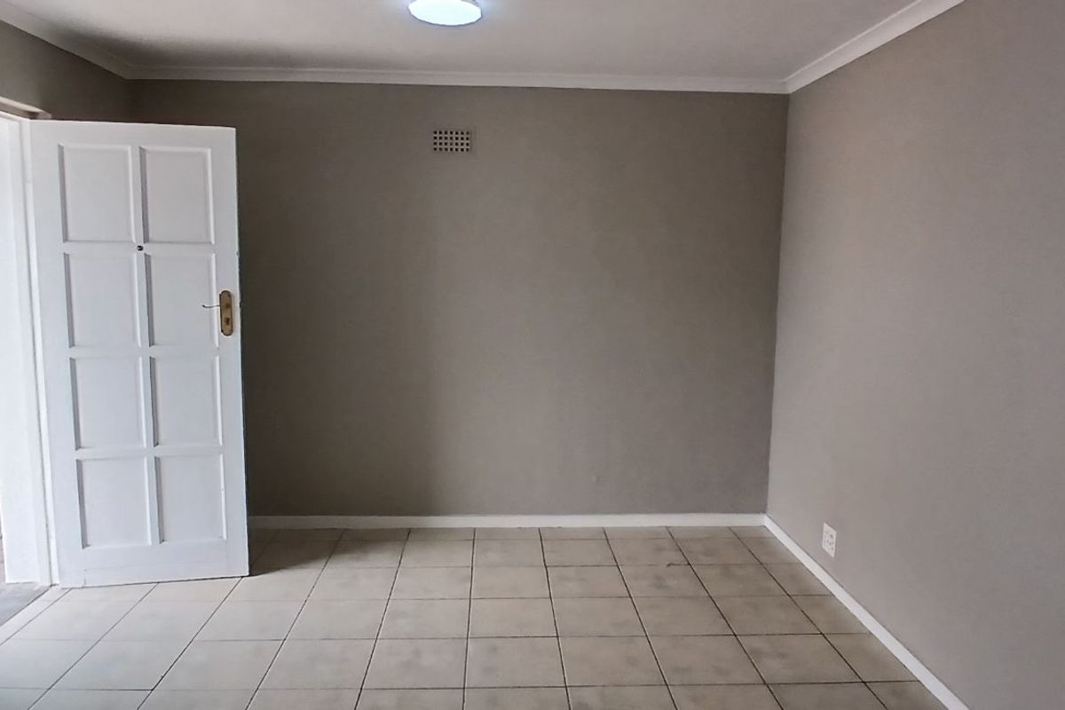 An empty living area featuring neutral wall paint, tiled flooring, and a view into the adjacent kitchen space.