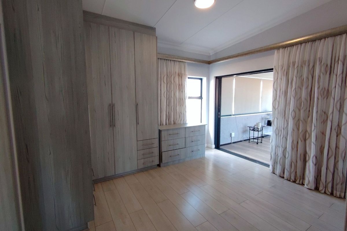 A well-maintained bedroom featuring built-in wooden cabinetry, light-toned flooring, and sliding glass doors leading to an adjacent space.