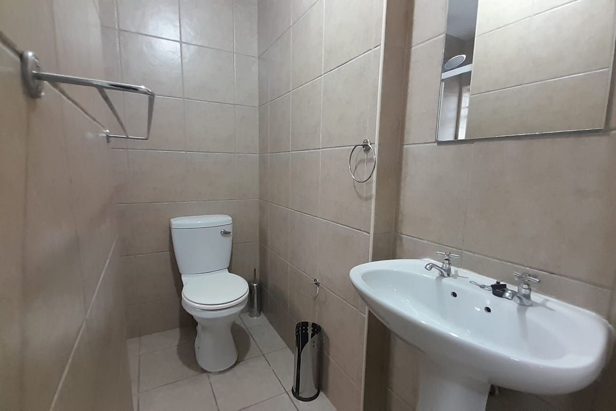 A functional bathroom featuring floor-to-ceiling wall tiles, a pedestal basin, and a standard toilet.